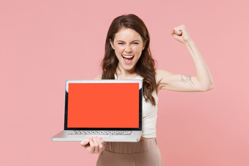 Happy young brunette woman girl in light casual clothes isolated on pink background. People lifestyle concept. Mock up copy space. Hold laptop pc computer with blank empty screen doing winner gesture.