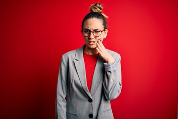Young beautiful blonde businesswoman with blue eyes wearing glasses and jacket touching mouth with hand with painful expression because of toothache or dental illness on teeth. Dentist