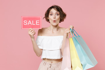 Fototapeta premium Amazed young woman girl in summer clothes isolated on pastel pink background studio portrait. Shopping discount sale concept. Mock up copy space. Hold package bag with purchases sign with SALE title.