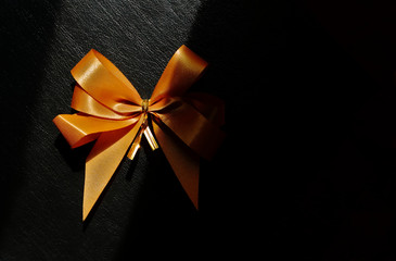 Closeup shiny golden tied bow on rough black surface, high angle view with sunlight and shadow 
