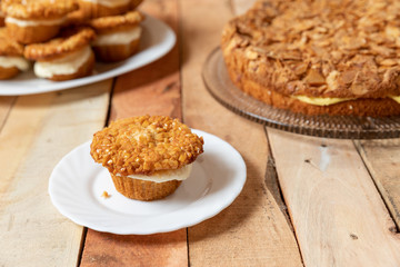 gebackener Bienenstich als Torte und Muffin mit Füllung aus Creme auf Tisch aus Holz