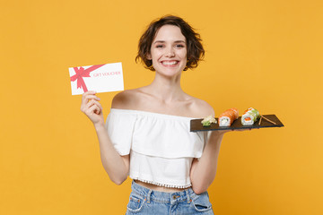 Young woman girl in casual clothes hold in hand gift certificate makizushi sushi roll served on plate traditional japanese food isolated on yellow background studio portrait. People lifestyle concept