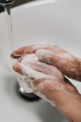 Fototapeta premium Washing hand with soap and foam, thorough cleaning to prevent coronavirus infection, in a stylish bathroom with a white sink, how to wash your hands close-up