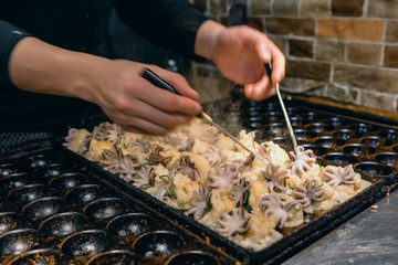 Chef is cooking Takoyaki, the most famous local street food in OSAKA with the black hot pan.