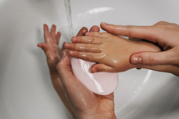 Naklejka premium mom washes her baby's hands thoroughly with soap and foam in the bathroom for hygiene purposes, hands closeup