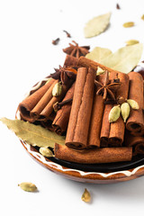 Healthy food ingredient mix of spices organic Cinnamon sticks, star anise, bay leaves and Cardamom pods in brown handle ceramic bowl on white background
