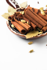 Healthy food ingredient mix of spices organic Cinnamon sticks, star anise, bay leaves and Cardamom pods in brown handle ceramic bowl on white background