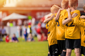 Kids sport team in yellow golden jerseys having pep talk with coach. Children soccer team motivated by trainer. Coaching football youth team. Young boys standing together united