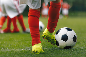 Football players feet close up. Sports training  on a grass field background. Boys in a sportswear. Players wearing red football socks and soccer cleats. Football horizontal background. Football kick