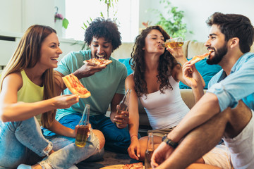 Group of multi ethnic young friends eating pizza at home and having fun.
