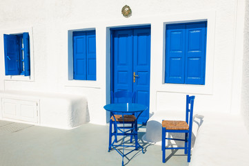 Traditional greek white architecture with blue doors and windows. Blue table with two chairs on the patio. Santorini island, Greece.