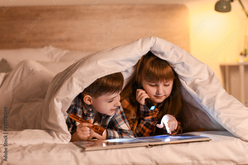 Wall mural Little children reading book under blanket at night