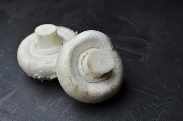 Raw cultivated champignon mushrooms on dark grey slate background. Vegitarian food cooking.