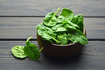 Spinach leaves in wooden bowl over wooden table background. Vegan food trend. Green living concept.