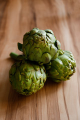 Fototapeta premium Fresh green Italian Artichoke natural wood background. Organic local produce vegetable on textured table. Vegan diet. Clean eating concept. Close up, top view, flat lay.