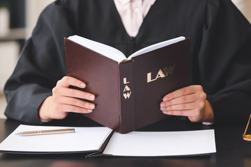 Female judge with law book at table in office, closeup