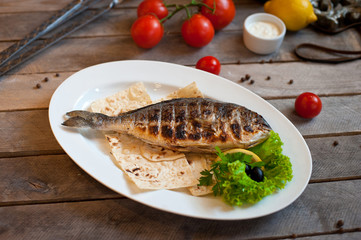 Fried fish Dorada, sea bream with spices, herbs and lemon fried on a grill on a white plate, top view