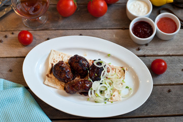 Meat kebab with onions on a white plate on a wooden background. Grilled meat