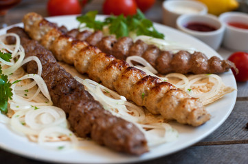 A portion of Lule kebab on a white plate with greens. A delicious dish on a brown wooden table. 