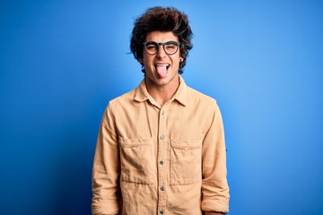 Young handsome man wearing casual shirt standing over isolated blue background sticking tongue out happy with funny expression. Emotion concept.