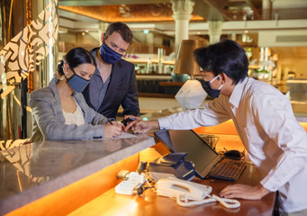 Couple and receptionist at counter in hotel wearing medical masks as precaution against virus. Couple on a business trip doing check-in at the hotel