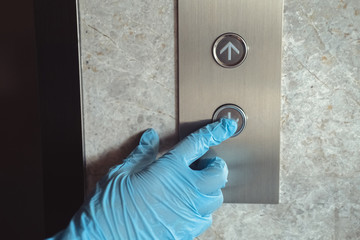A hand wearing protective rubber gloves is pressing elevator button. Infection prevention and control of Corona virus Covid-19 epidemic. © Space_Cat