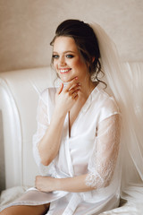 Fototapeta premium Close-up portrait of a bride in a bathrobe. A young girl of European appearance, with makeup, hairstyle and veil in a boudoir.