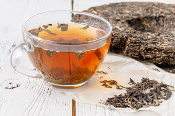 A cup of Chinese tea is next to a large piece of puer