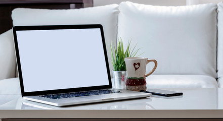 Mockup blank screen laptop with smartphone, mug and houseplant on white wooden top table in living room.
