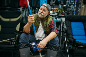 Fototapeta na wymiar Angler in rubber boots holds rod in fishing shop