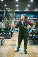 Angler in rubber jumpsuit holds net, fishing shop
