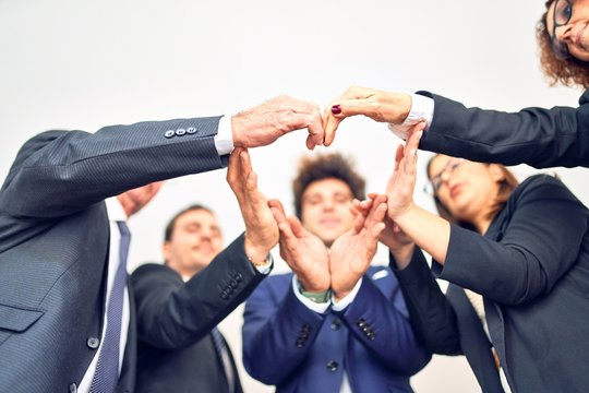 Group of business workers smiling happy and confident. Standing on a circle with smile on face doing symbol with hands and arms together at the office.