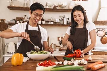 Image of young multicultural couple in aprons laughing and making lunch