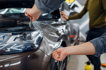 Worker applies car protection film on front fender