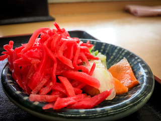 Close up of Beni shoga on small plate. It is made from thin strips of ginger pickled in umezu, the pickling solution used to make umeboshi. The red color is traditionally derived from red perilla