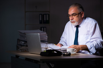 Obraz premium Old male employee working late at workplace