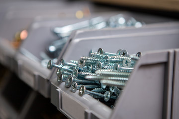 Focus on white silver screws in plastic boxes located on a shelf in a tool and accessories store....