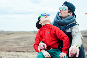 young father with his son having fun outside in spring field, happy family smiling, lifestyle people making selfie wearing sunglasses