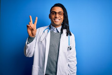 Young african american doctor man with dreadlocks wearing stethoscope and glasses smiling with happy face winking at the camera doing victory sign. Number two.