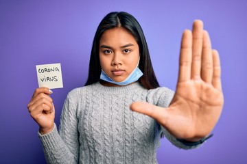 Asian girl wearing medical mask asking for alert holding reminder with corona virus message with open hand doing stop sign with serious and confident expression, defense gesture © Krakenimages.com