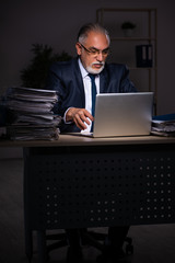 Old male employee working late at workplace