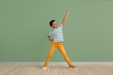 Little African-American boy dancing against color wall