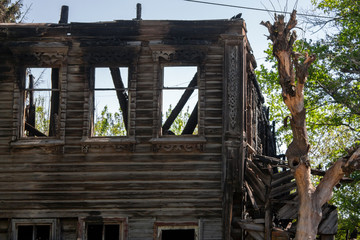 Obraz premium The ruins of a wooden house after a fire. Burnt logs of a two-story building after a fire. Through the broken windows you can see the sky in the ruined house.