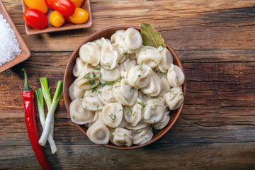 homemade dumplings with sour cream and dill on a wooden vintage table with fresh tomatoes, onions and spices