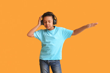 Little African-American boy listening to music and dancing against color background