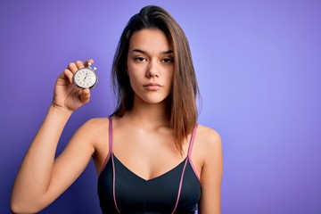 Young beautiful sporty girl doing sport using stopwatch over isolated purple background with a confident expression on smart face thinking serious