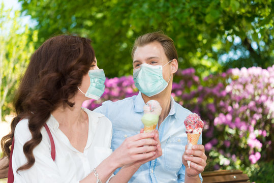 Young Couple Eating An Ice Cream Outdoor While Wearing A Coronavirus Mask