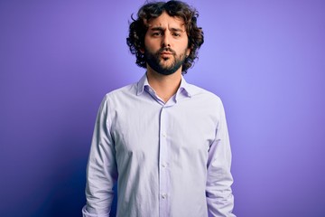 Young handsome business man with beard wearing shirt standing over purple background looking at the camera blowing a kiss on air being lovely and sexy. Love expression.
