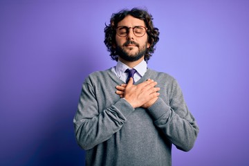 Handsome businessman with beard wearing tie and glasses standing over purple background smiling with hands on chest with closed eyes and grateful gesture on face. Health concept.