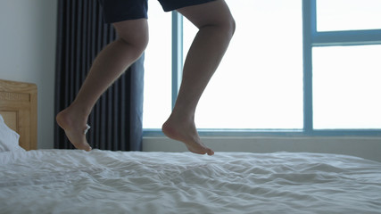 Man have fun, jumping, dancing on bed by the window. Close up of his feet